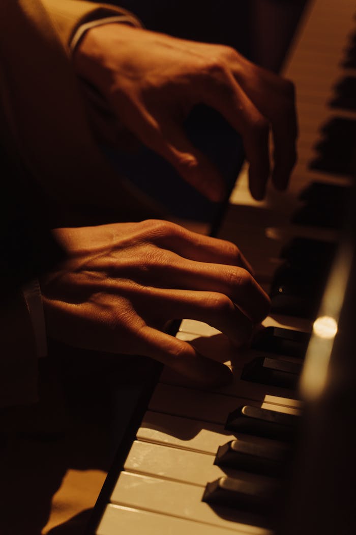 Close-up of a musician's hands gracefully playing a piano in warm lighting.